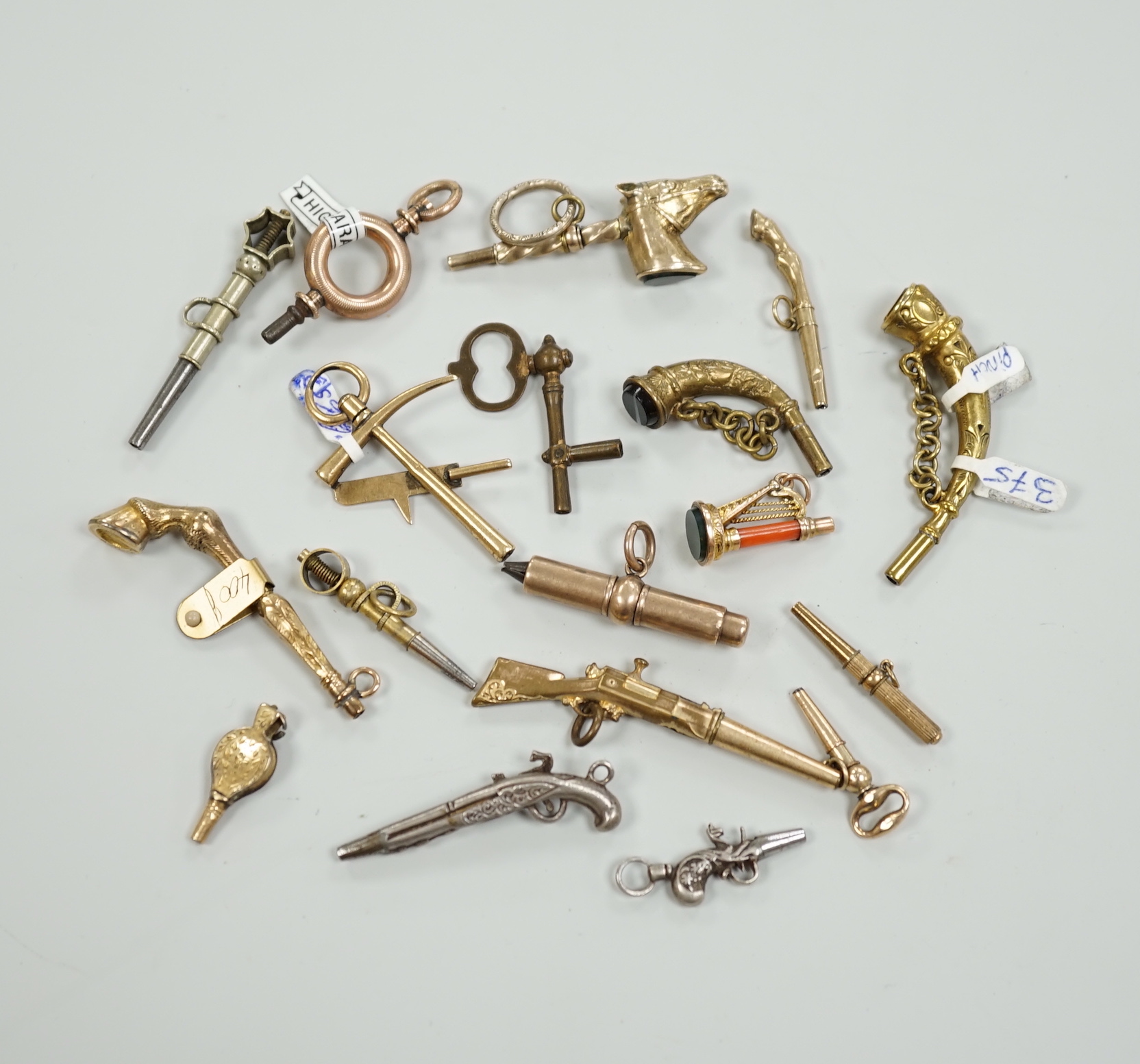 Eighteen assorted mainly 19th century base or yellow metal overlaid novelty watch keys, including coral and bloodstone set harp, pistol, rifle, cornucopia, bellows, horses hoof and trade insignia, largest 55mm.